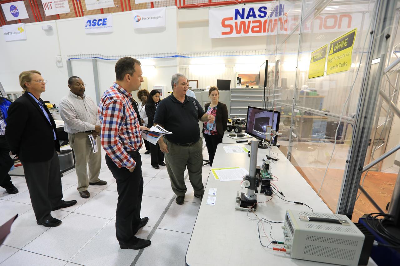 Thomas Zurbuchen, in plaid shirt, NASA's associate administrator for the Science Mission Directorate, listens to a presentation at the Swamp Works facility at NASA's Kennedy Space Center in Florida. In the foreground is a prototype robotic exploration vehicle.