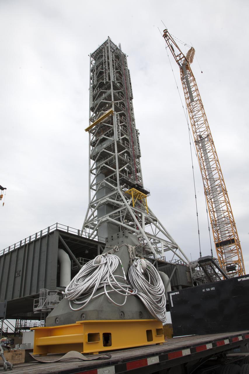 A flatbed truck carries a vertical support post (VSP) for NASA's Space Launch System (SLS) rocket to the Mobile Launcher Yard at NASA's Kennedy Space Center in Florida. In view is the mobile launcher. The two aft skirt electrical umbilicals (ASEUs) and the first of the vehicle support posts underwent a series of tests to confirm they are functioning properly and ready to support the SLS for launch. The ASEUs will connect to the SLS rocket at the bottom outer edge of each booster and provide electrical power and data connections to the rocket until it lifts off from the launch pad. The eight VSPs will support the load of the solid rocket boosters, with four posts for each of the boosters. The center’s Engineering Directorate and the Ground Systems Development and Operations Program are overseeing processing and testing of the umbilicals.