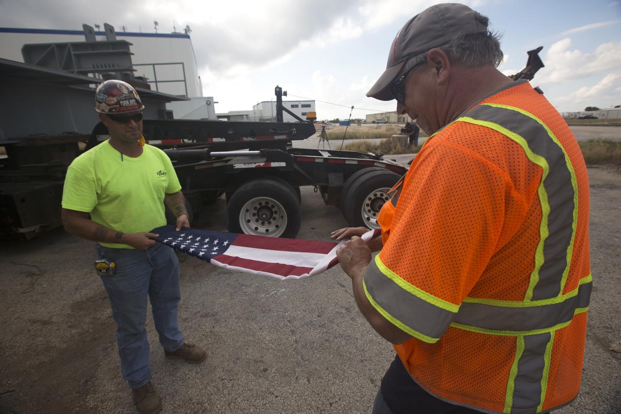 Workers fold an American flag that was on the back of a heavy load transport truck from Tillett Heavy Hauling in Titusville, Florida. The truck arrived at the Vehicle Assembly Building (VAB) at NASA’s Kennedy Space Center in Florida, carrying the second half of the A-level work platforms, A north, for the agency’s Space Launch System (SLS) rocket. This is the final platform delivered to Kennedy. The A-level platforms are the topmost platforms for High Bay 3 in the Vehicle Assembly Building (VAB). The platform will be delivered to the VAB staging area in the west parking lot. The Ground Systems Development and Operations Program is overseeing upgrades and modifications to High Bay 3 to support processing of the SLS and Orion spacecraft. A total of 10 levels of new platforms, 20 platform halves altogether, will surround the SLS rocket and Orion spacecraft and provide access for testing and processing.