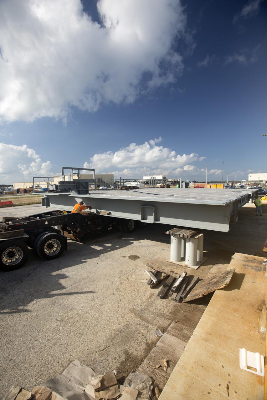 Blue sky and fluffy clouds serve as the backdrop for the arrival of the second half of the A-level work platforms, A north, for the NASA's Space Launch System (SLS) rocket near the Vehicle Assembly Building (VAB) at NASA's Kennedy Space Center in Florida. Workers prepare to offload the platform from a heavy load transport truck from Tillett Heavy Hauling in Titusville, Florida, to a staging area near the VAB. This is the final platform delivered to Kennedy. The A-level platforms are the topmost platforms for High Bay 3 in the Vehicle Assembly Building (VAB). The Ground Systems Development and Operations Program is overseeing upgrades and modifications to High Bay 3 to support processing of the SLS and Orion spacecraft. A total of 10 levels of new platforms, 20 platform halves altogether, will surround the SLS rocket and Orion spacecraft and provide access for testing and processing. 