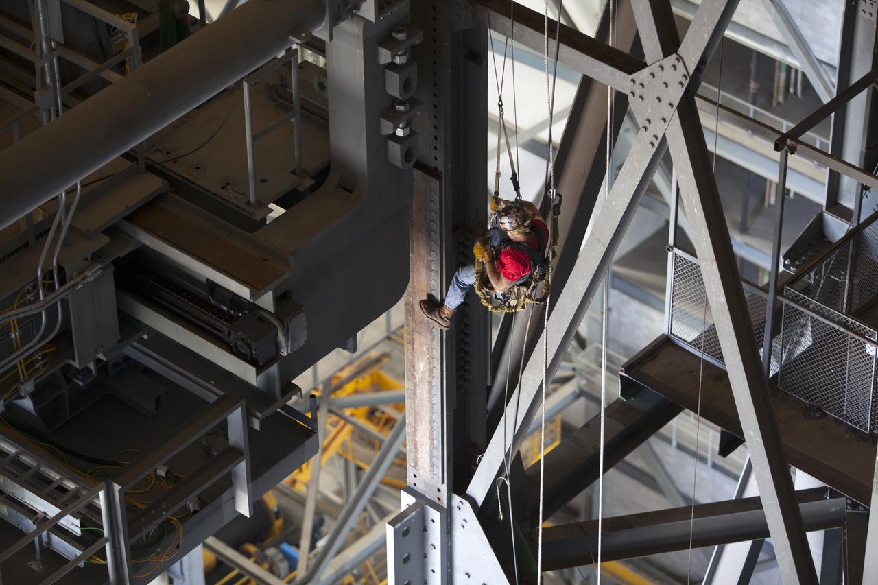 A construction worker wearing a safety harness and tethered lines monitors the progress during the installation of the second half of the B-level work platforms, B north, for NASA’s Space Launch System (SLS) rocket, high up in the Vehicle Assembly Building (VAB) at NASA’s Kennedy Space Center in Florida.  The B platform will be installed on the north side of High Bay 3. The B platforms are the ninth of 10 levels of work platforms that will surround and provide access to the SLS rocket and Orion spacecraft for Exploration Mission 1. The Ground Systems Development and Operations Program is overseeing upgrades and modifications to VAB High Bay 3, including installation of the new work platforms, to prepare for NASA’s Journey to Mars.