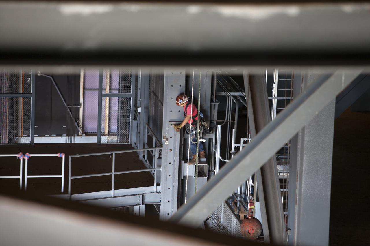 A construction worker wearing a safety harness and tethered lines monitors the progress during the installation of the second half of the B-level work platforms, B north, for NASA’s Space Launch System (SLS) rocket, high up in the Vehicle Assembly Building (VAB) at NASA’s Kennedy Space Center in Florida.  The B platform will be installed on the north side of High Bay 3. The B platforms are the ninth of 10 levels of work platforms that will surround and provide access to the SLS rocket and Orion spacecraft for Exploration Mission 1. The Ground Systems Development and Operations Program is overseeing upgrades and modifications to VAB High Bay 3, including installation of the new work platforms, to prepare for NASA’s Journey to Mars. 