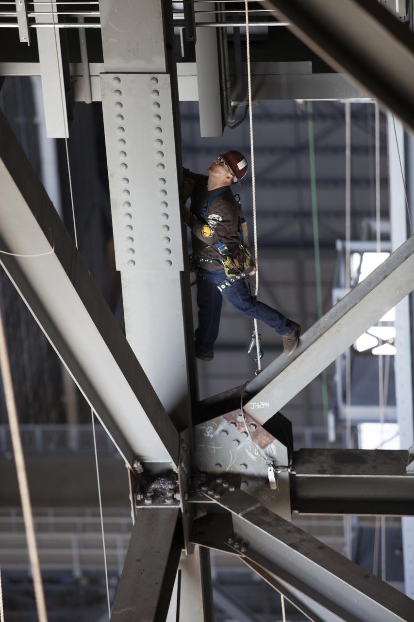 A construction worker wearing a safety harness and tethered lines prepares to assist with the installation of the second half of the B-level work platforms, B north, for NASA’s Space Launch System (SLS) rocket, high up in the Vehicle Assembly Building (VAB) at NASA’s Kennedy Space Center in Florida. The B platform will be installed on the north side of High Bay 3. The B platforms are the ninth of 10 levels of work platforms that will surround and provide access to the SLS rocket and Orion spacecraft for Exploration Mission 1. The Ground Systems Development and Operations Program is overseeing upgrades and modifications to VAB High Bay 3, including installation of the new work platforms, to prepare for NASA’s Journey to Mars. 