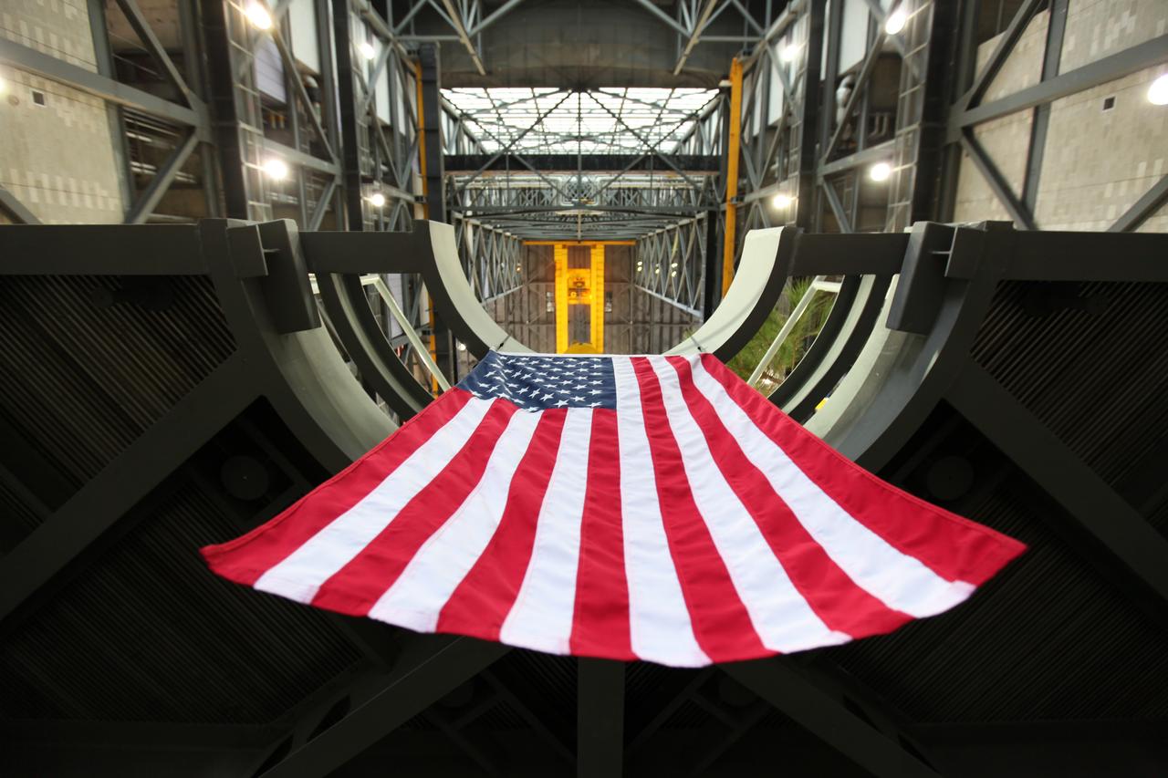 In a view from below, the American flag is in view hanging from the final work platform, A north, as the platform is lifted up by crane from the transfer aisle in the Vehicle Assembly Building (VAB) at NASA's Kennedy Space Center in Florida. The platform will be installed and secured on its rail beam high up on the north wall of High Bay 3. The installation of the final topmost level completes the 10 levels of work platforms, 20 platform halves altogether, that will surround NASA's Space Launch System rocket and the Orion spacecraft and allow access during processing for missions, including the first uncrewed flight test of Orion atop the SLS rocket in 2018. The A-level platforms will provide access to the Orion spacecraft's Launch Abort System for Orion lifting sling removal and installation of the closeout panels. The Ground Systems Development and Operations Program, with support from the center's Engineering Directorate, is overseeing upgrades and modifications to the VAB, including installation of the new work platforms.