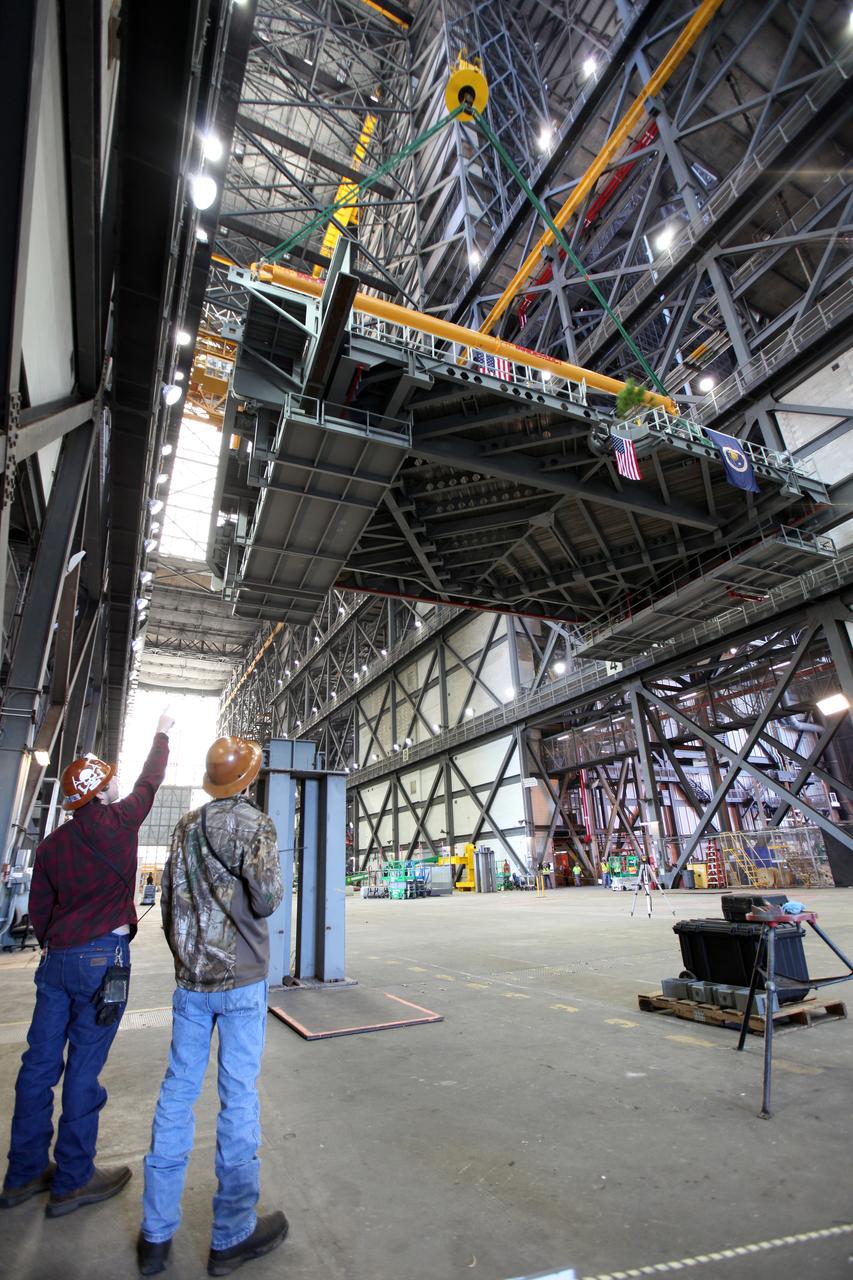 Construction workers watch as a crane begins to lift the final work platform, A north, in the transfer aisle of the Vehicle Assembly Building (VAB) at NASA's Kennedy Space Center in Florida. The platform will be installed and secured on its rail beam high up on the north wall of High Bay 3. The installation of the final topmost level completes the 10 levels of work platforms, 20 platform halves altogether, that will surround NASA's Space Launch System rocket and the Orion spacecraft and allow access during processing for missions, including the first uncrewed flight test of Orion atop the SLS rocket in 2018. The A-level platforms will provide access to the Orion spacecraft's Launch Abort System for Orion lifting sling removal and installation of the closeout panels. The Ground Systems Development and Operations Program, with support from the center's Engineering Directorate, is overseeing upgrades and modifications to the VAB, including installation of the new work platforms. 