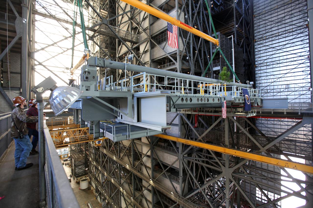 Construction workers watch as a crane lifts the final work platform, A north, high up from the transfer aisle in the Vehicle Assembly Building (VAB) at NASA's Kennedy Space Center in Florida. The platform will be installed and secured on its rail beam high up on the north wall of High Bay 3. The installation of the final topmost level completes the 10 levels of work platforms, 20 platform halves altogether, that will surround NASA's Space Launch System rocket and the Orion spacecraft and allow access during processing for missions, including the first uncrewed flight test of Orion atop the SLS rocket in 2018. The A-level platforms will provide access to the Orion spacecraft's Launch Abort System for Orion lifting sling removal and installation of the closeout panels. The Ground Systems Development and Operations Program, with support from the center's Engineering Directorate, is overseeing upgrades and modifications to the VAB, including installation of the new work platforms. 