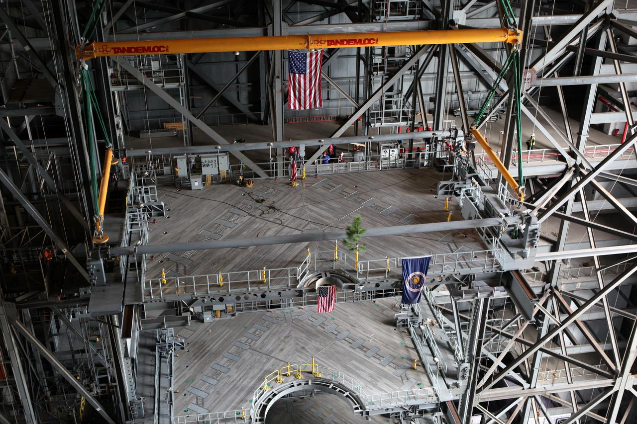 High up in the Vehicle Assembly Building (VAB) at NASA's Kennedy Space Center in Florida, a crane lowers the final work platform, A north, for installation in High Bay 3. The platform will be installed and secured on its rail beam high up on the north wall of the high bay. In view on the platform are the American flag and a small tree. The installation of the final topmost level completes the 10 levels of work platforms, 20 platform halves altogether, that will surround NASA's Space Launch System rocket and the Orion spacecraft and allow access during processing for missions, including the first uncrewed flight test of Orion atop the SLS rocket in 2018. The A-level platforms will provide access to the Orion spacecraft's Launch Abort System for Orion lifting sling removal and installation of the closeout panels. The Ground Systems Development and Operations Program, with support from the center's Engineering Directorate, is overseeing upgrades and modifications to the VAB, including installation of the new work platforms. 