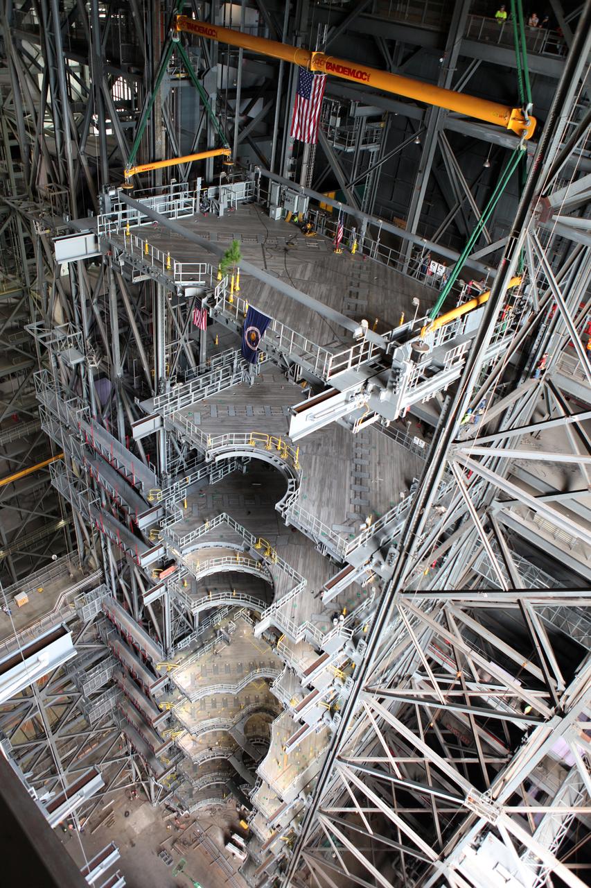 High up in the Vehicle Assembly Building (VAB) at NASA's Kennedy Space Center in Florida, a crane lowers the final work platform, A north, for installation in High Bay 3. The platform will be installed and secured on its rail beam high up on the north wall of the high bay. In view on the platform are the American flag and a small tree. In view below are the nine previously installed platforms. The installation of the final topmost level completes the 10 levels of work platforms, 20 platform halves altogether, that will surround NASA's Space Launch System rocket and the Orion spacecraft and allow access during processing for missions, including the first uncrewed flight test of Orion atop the SLS rocket in 2018. The A-level platforms will provide access to the Orion spacecraft's Launch Abort System for Orion lifting sling removal and installation of the closeout panels. The Ground Systems Development and Operations Program, with support from the center's Engineering Directorate, is overseeing upgrades and modifications to the VAB, including installation of the new work platforms.