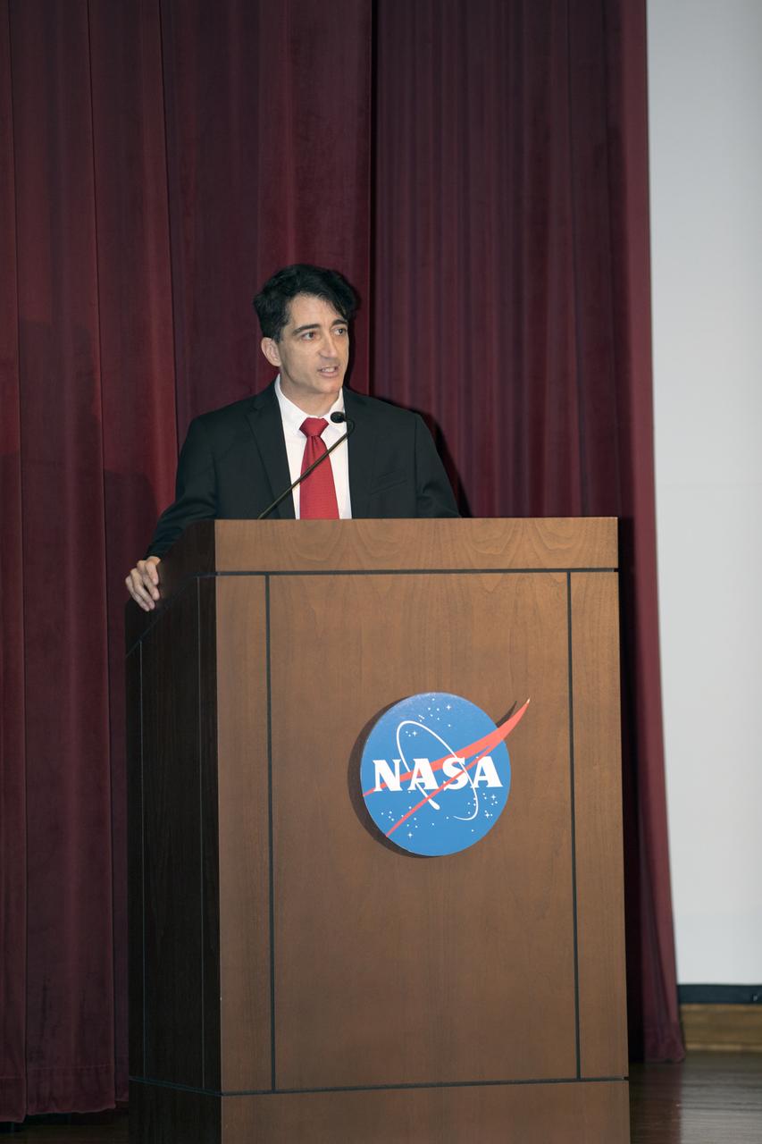 Mike Ciannilli, the Apollo, Challenger, Columbia Lessons Learned Program manager, welcomes participants to the Apollo 1 Lessons Learned presentation in the Training Auditorium at NASA’s Kennedy Space Center in Florida. The program's theme was "To There and Back Again." Guest panelists included Charlie Duke, former Apollo 16 astronaut and member of the Apollo 1 Emergency Egress Investigation Team; Ernie Reyes, retired, Apollo 1 senior operations engineer; and John Tribe, retired, Apollo 1 Reaction and Control System lead engineer. The event helped pay tribute to the Apollo 1 crew, Gus Grissom, Ed White II, and Roger Chaffee.