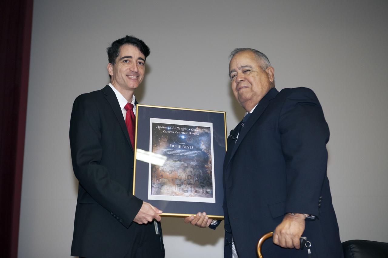Mike Ciannilli, the Apollo, Challenger, Columbia Lessons Learned program manager, at left, presents a certificate to Ernie Reyes, retired, former Apollo 1 senior operations manager, during the Apollo 1 Lessons Learned presentation in the Training Auditorium at NASA's Kennedy Space Center in Florida. The theme of the program was "To there and Back Again." The event helped pay tribute to the Apollo 1 crew, Gus Grissom, Ed White II, and Roger Chaffee.