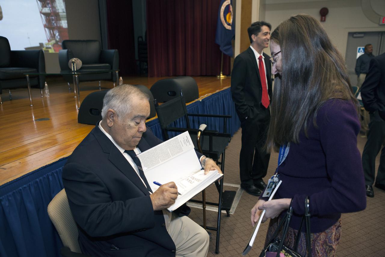 Ernie Reyes, retired, former Apollo 1 senior operations manager, signs a book for a worker after the Apollo 1 Lessons Learned presentation in the Training Auditorium at NASA's Kennedy Space Center in Florida. The theme of the program was "To there and Back Again." The event helped pay tribute to the Apollo 1 crew, Gus Grissom, Ed White II, and Roger Chaffee.