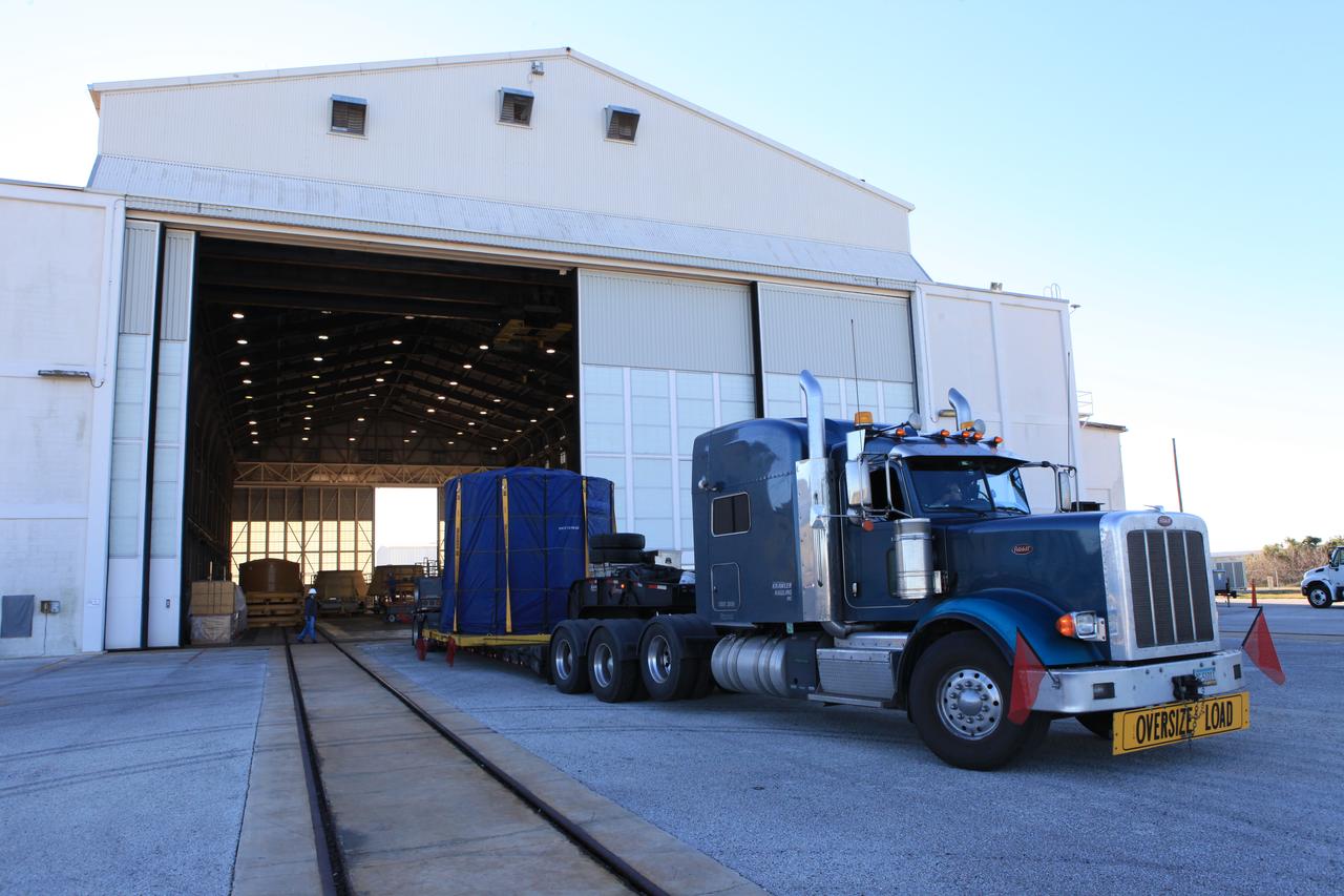 A flatbed truck carrying the left-hand forward skirt for NASA's Space Launch System (SLS) solid rocket boosters arrives at the Hangar AF facility at Cape Canaveral Air Force Station in Florida. The forward skirt was transported from booster prime contractor Orbital ATK in Promontory, Utah. The forward skirt will be staged in Hangar AF where refurbishment will continue. It will be inspected and prepared for use on the left-hand solid rocket booster for Exploration Mission 1. NASA's Orion spacecraft will fly atop the SLS rocket on its first uncrewed flight test.