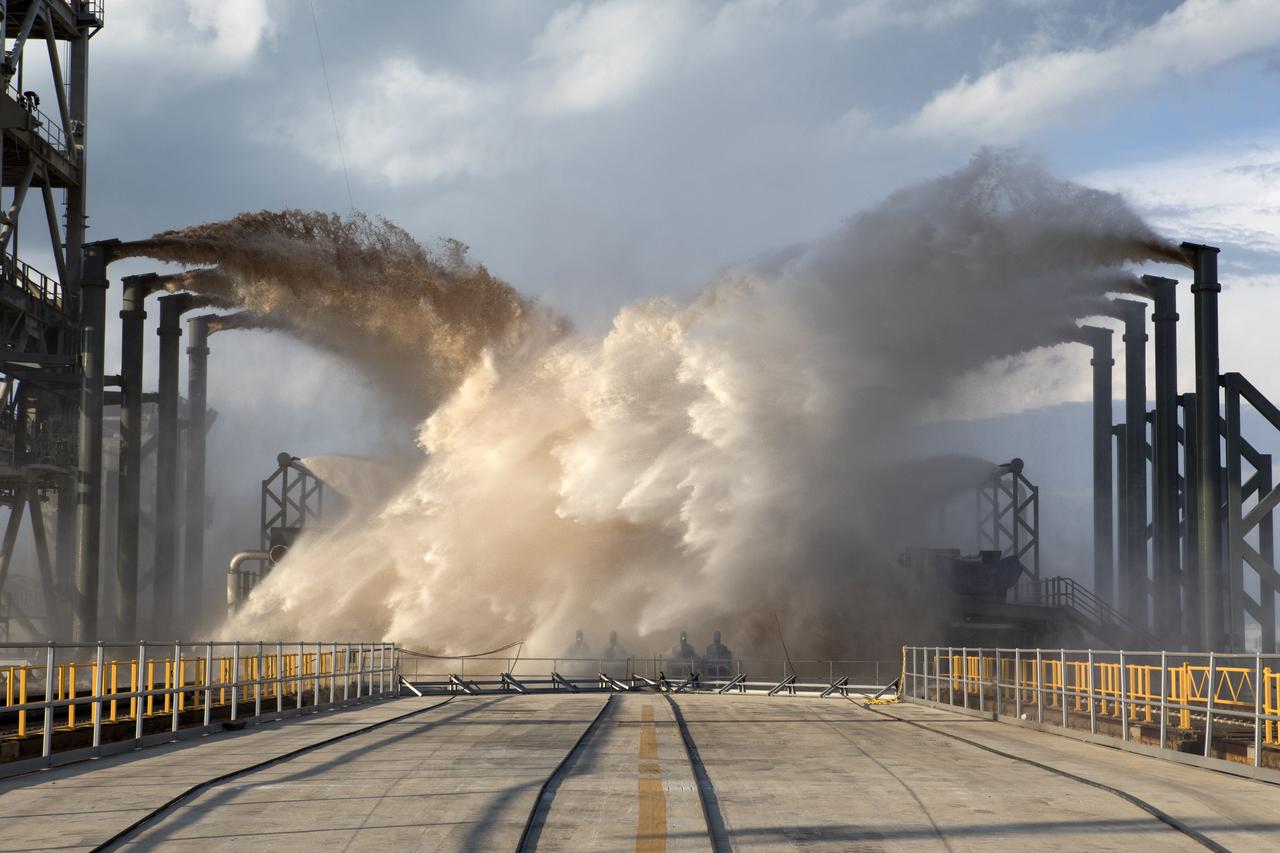 Water sprays onto Launch Complex 39A during a test by SpaceX of the sound suppression system at the launch pad. The water deluge diminishes vibration at the pad during a liftoff to protect the pad structures and rocket itself from excessive shaking. Photo credit: NASA/Kim Shiflett