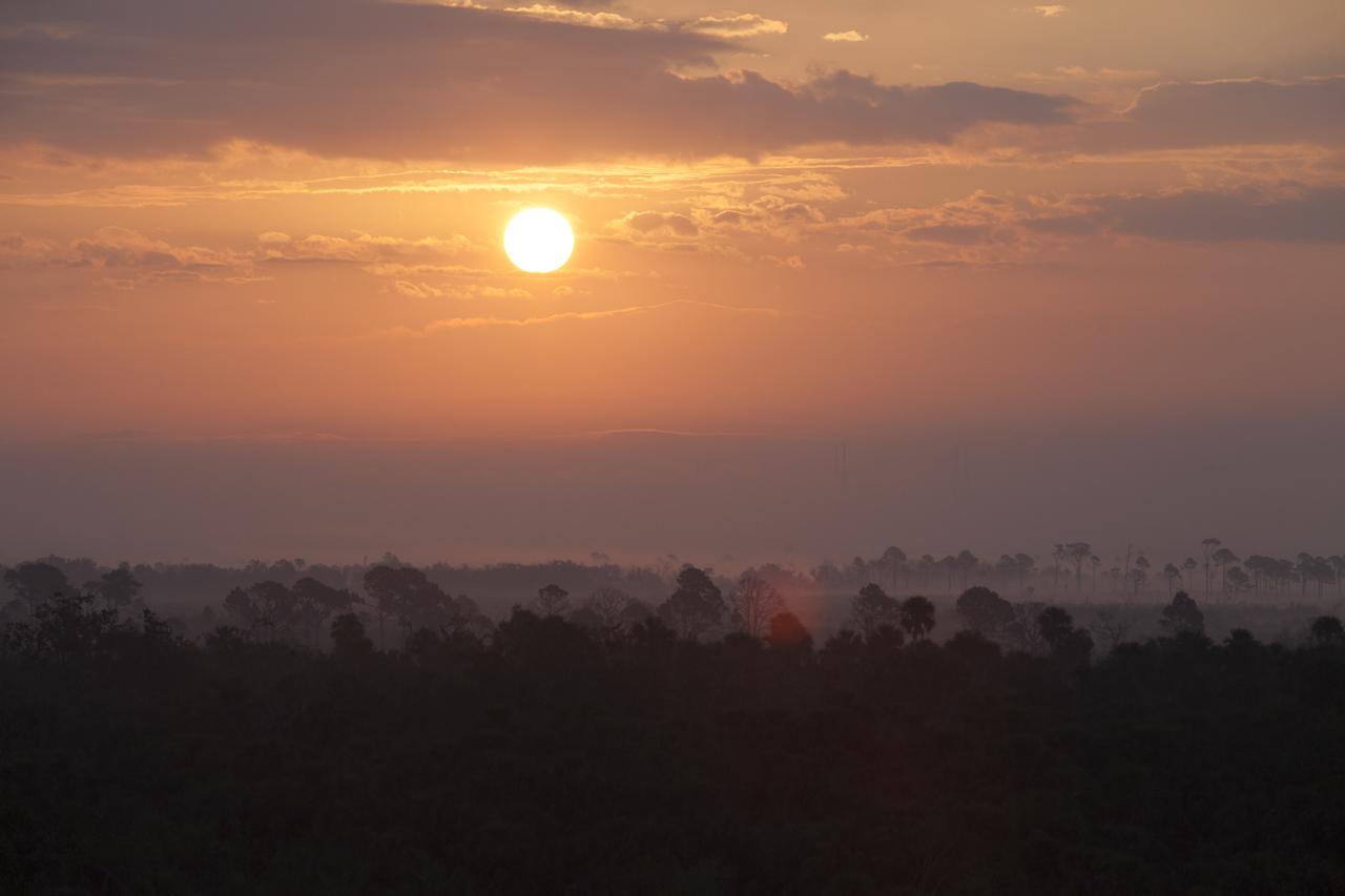 A sunrise view from the observation deck of the Operations and Support Building II at NASA's Kennedy Space Center in Florida, as a SpaceX Falcon 9 rocket awaits launch from Launch Complex 39A. It is the company's 10th commercial resupply services mission to the International Space Station. The Dragon spacecraft will deliver about 5,500 pounds of supplies to the space station. 