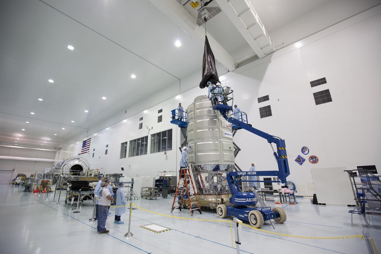 In the Space Station Processing Facility high bay at NASA's Kennedy Space Center in Florida, technicians assist as a crane is used to lower a protective covering around Orbital ATK's CYGNUS pressurized cargo module. The Orbital ATK CRS-7 commercial resupply services mission to the International Space Station is scheduled to launch atop a United Launch Alliance Atlas V rocket from Space Launch Complex 41 at Cape Canaveral Air Force Station on March 19, 2017. CYGNUS will deliver thousands of pounds of supplies, equipment and scientific research materials to the space station.