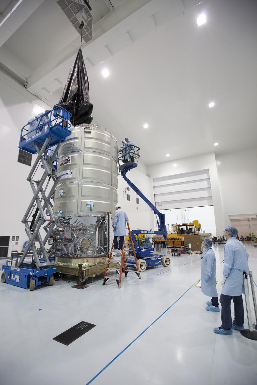 In the Space Station Processing Facility high bay at NASA's Kennedy Space Center in Florida, technicians assist as a crane is used to lower a protective covering around Orbital ATK's CYGNUS pressurized cargo module. The Orbital ATK CRS-7 commercial resupply services mission to the International Space Station is scheduled to launch atop a United Launch Alliance Atlas V rocket from Space Launch Complex 41 at Cape Canaveral Air Force Station on March 19, 2017. CYGNUS will deliver thousands of pounds of supplies, equipment and scientific research materials to the space station.