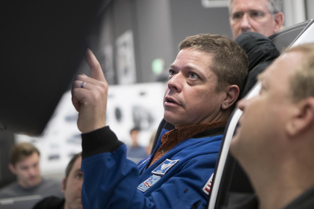 During a tour of SpaceX headquarters in Hawthorne, California, commercial crew astronauts Bob Behnken, left, and Eric Boe participate in joint test team training using mockup components of the Crew Dragon on Feb. 23, 2017. Mike Good, program manager for Crew Operations and Testing at Johnson Space Center in Houston, is in the background. Crew Dragon is being developed and manufactured in partnership with NASA's Commercial Crew Program to return human spaceflight capabilities to the U.S.