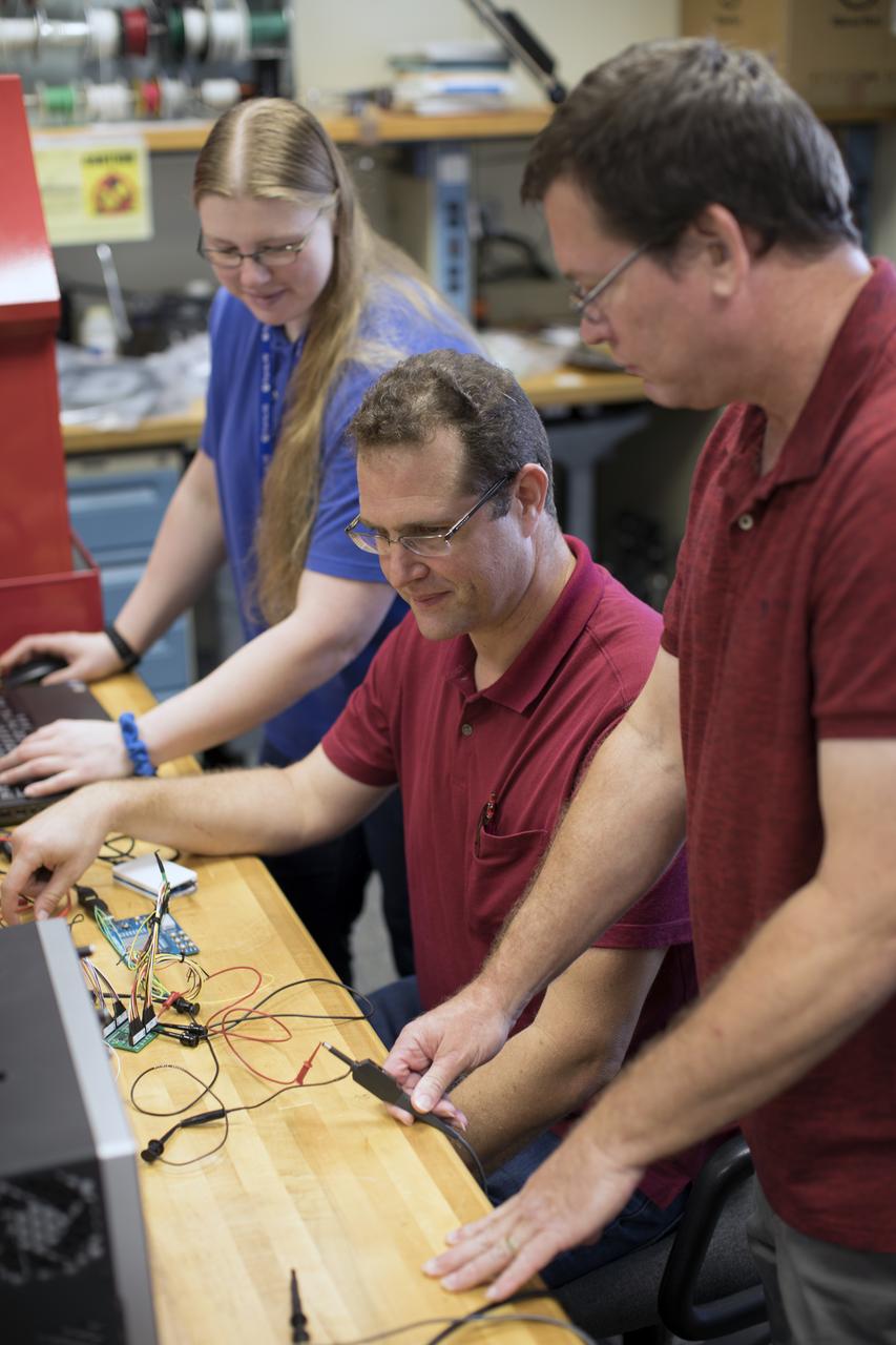 Jamie Szafran, from left, Mark Lewis and Curtis Ihlefeld work with the prototype of the Flexible Damage Detection System in a laboratory with a prototype at NASA's Kennedy Space Center in Florida. The system uses circuits printed on thin thermal film and specialized software. The system is designed to show where damage to a surface occurs and how severe it may be. It could offer astronauts a real-time update on their spacecraft's condition during a mission without requiring a spacewalk. 