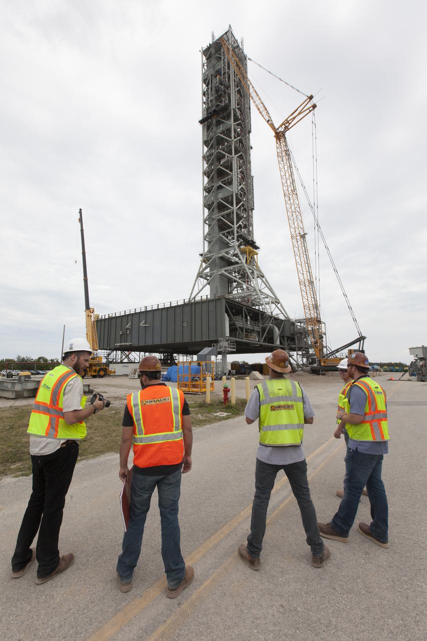 Crane specialists monitor the progress as the bracket for the Orion Service Module Umbilical (OSMU) is lifted high up for installation on the mobile launcher tower at NASA's Kennedy Space Center in Florida. The mobile launcher tower will be equipped with a number of lines, called umbilicals, that will connect to the Space Launch System rocket and Orion spacecraft for Exploration Mission-1 (EM-1). The OSMU will be located high on the mobile launcher tower and, prior to launch, will transfer liquid coolant for the electronics and air for the Environmental Control System to the Orion service module that houses these critical systems to support the spacecraft. EM-1 is scheduled to launch in 2018. The Ground Systems Development and Operations Program is overseeing installation of the umbilicals.