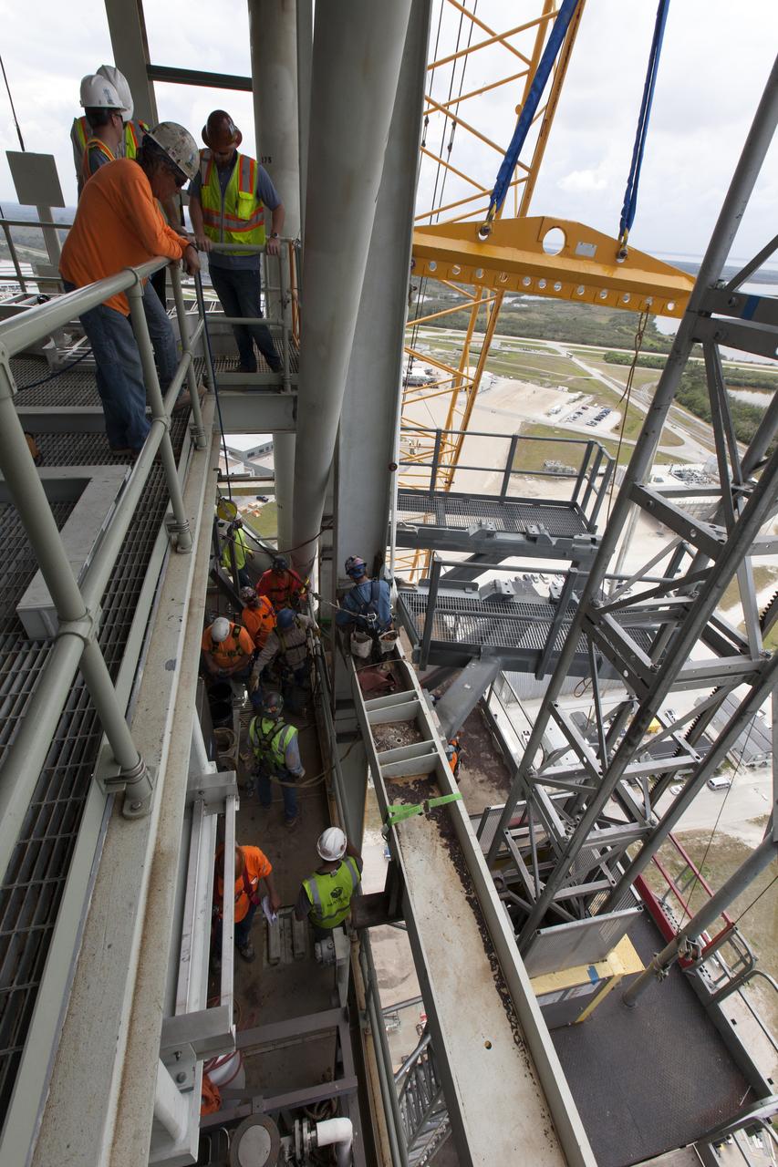 Construction workers and crane specialists high up on the mobile launcher tower monitor the progress as a crane positions the bracket for the Orion Service Module Umbilical (OSMU) for installation on the mobile launcher tower at NASA's Kennedy Space Center in Florida. The tower will be equipped with a number of lines, called umbilicals, that will connect to the Space Launch System rocket and Orion spacecraft for Exploration Mission-1 (EM-1). The OSMU will be located high on the mobile launcher tower and, prior to launch, will transfer liquid coolant for the electronics and air for the Environmental Control System to the Orion service module that houses these critical systems to support the spacecraft. EM-1 is scheduled to launch in 2018. The Ground Systems Development and Operations Program is overseeing installation of the umbilicals. 