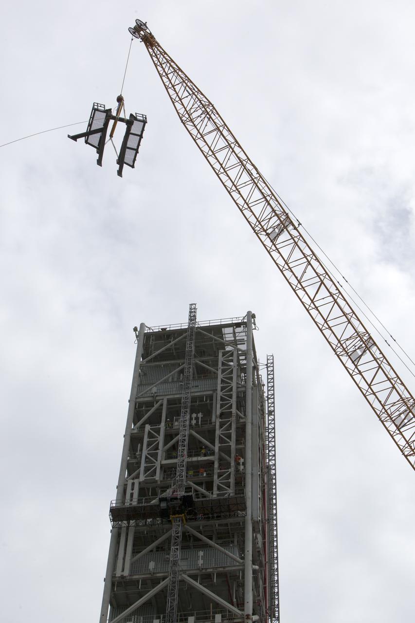 A crane lifts the bracket for the Orion Service Module Umbilical (OSMU) high up for installation on the mobile launcher tower at NASA's Kennedy Space Center in Florida. The mobile launcher tower will be equipped with a number of lines, called umbilicals, that will connect to the Space Launch System rocket and Orion spacecraft for Exploration Mission-1 (EM-1). The OSMU will be located high on the mobile launcher tower and, prior to launch, will transfer liquid coolant for the electronics and air for the Environmental Control System to the Orion service module that houses these critical systems to support the spacecraft. EM-1 is scheduled to launch in 2018. The Ground Systems Development and Operations Program is overseeing installation of the umbilicals.
