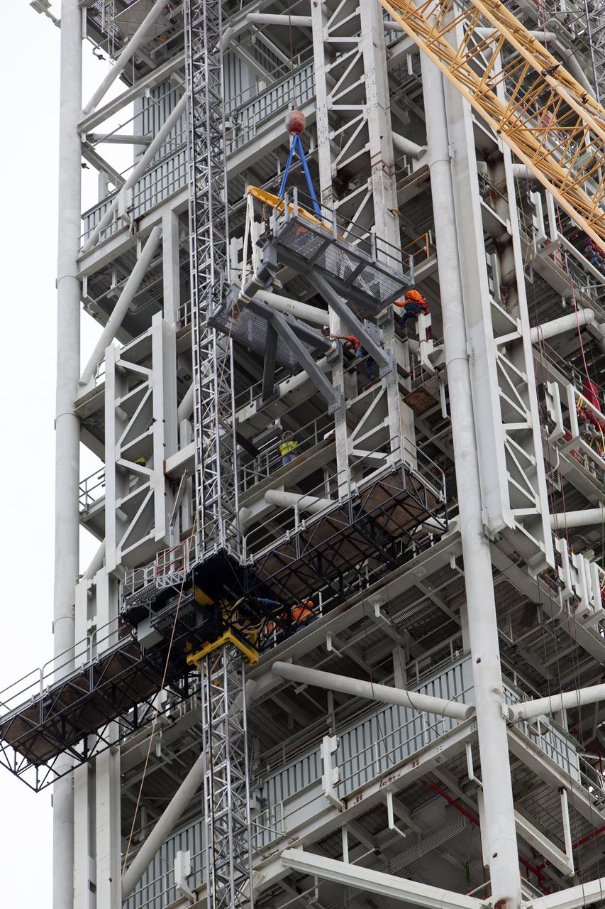 A crane positions the bracket for the Orion Service Module Umbilical (OSMU) for installation on the mobile launcher tower at NASA's Kennedy Space Center in Florida. The mobile launcher tower will be equipped with a number of lines, called umbilicals, that will connect to the Space Launch System rocket and Orion spacecraft for Exploration Mission-1 (EM-1). The OSMU will be located high on the mobile launcher tower and, prior to launch, will transfer liquid coolant for the electronics and air for the Environmental Control System to the Orion service module that houses these critical systems to support the spacecraft. EM-1 is scheduled to launch in 2018. The Ground Systems Development and Operations Program is overseeing installation of the umbilicals.