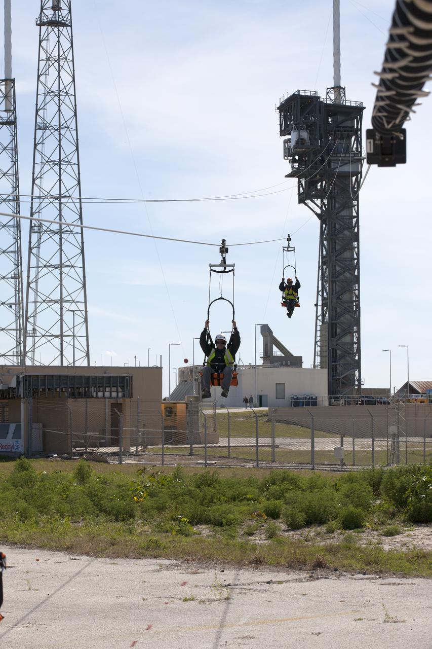 Two engineers evaluate the Emergency Egress System as they ride in folding seats attached to slide wires at Space Launch Complex 41. United Launch Alliance and Boeing continue modifications to the pad in order to host missions by the Boeing CST-100 Starliner carrying astronauts and crew. The system recently completed its final test. In the unlikely event of an emergency prior to liftoff, each person on the Crew Access Tower would get into their own seat attached to the wire and slide more than 1,340 feet to a safe area. The wires are situated 172 feet above the pad deck on level 12 of the tower. The Starliner will launch on a ULA Atlas V on mission to low-Earth orbit including those flying astronauts to the International Space Station during missions by NASA's Commercial Crew Program.