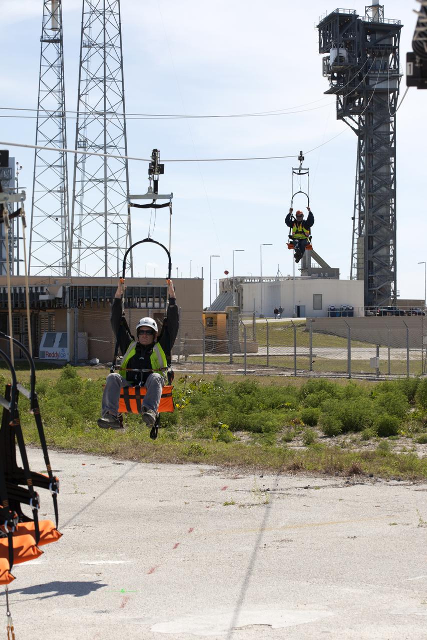 Two engineers evaluate the Emergency Egress System as they ride in folding seats attached to slide wires at Space Launch Complex 41. United Launch Alliance and Boeing continue modifications to the pad in order to host missions by the Boeing CST-100 Starliner carrying astronauts and crew. The system recently completed its final test. In the unlikely event of an emergency prior to liftoff, each person on the Crew Access Tower would get into their own seat attached to the wire and slide more than 1,340 feet to a safe area. The wires are situated 172 feet above the pad deck on level 12 of the tower. The Starliner will launch on a ULA Atlas V on mission to low-Earth orbit including those flying astronauts to the International Space Station during missions by NASA's Commercial Crew Program.