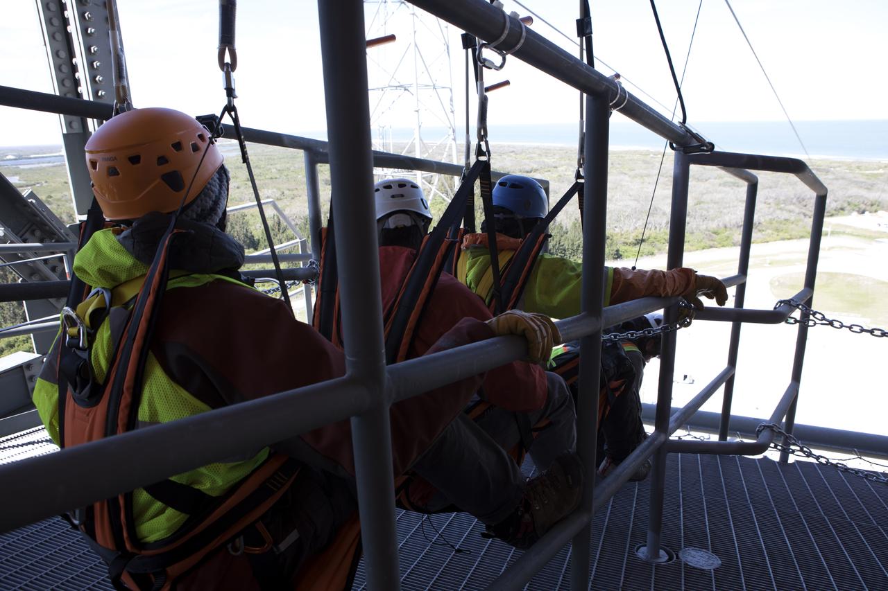 Three engineers prepare to evaluate the Emergency Egress System as they ride in folding seats attached to slide wires at Space Launch Complex 41. United Launch Alliance and Boeing continue modifications to the pad in order to host missions by the Boeing CST-100 Starliner carrying astronauts and crew. The system recently completed its final test. In the unlikely event of an emergency prior to liftoff, each person on the Crew Access Tower would get into their own seat attached to the wire and slide more than 1,340 feet to a safe area. The wires are situated 172 feet above the pad deck on level 12 of the tower. The Starliner will launch on a ULA Atlas V on mission to low-Earth orbit including those flying astronauts to the International Space Station during missions by NASA's Commercial Crew Program.