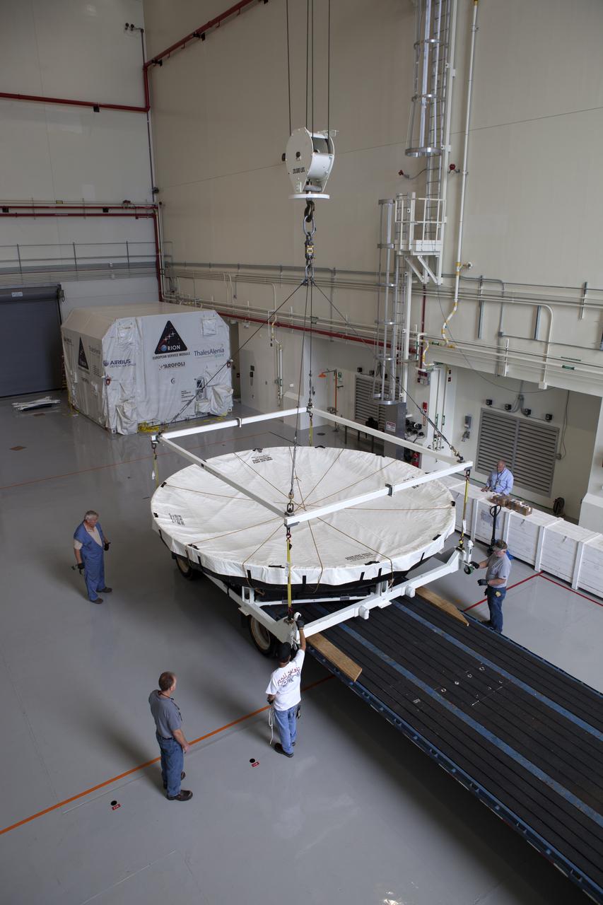 Inside the Launch Abort System Facility at NASA's Kennedy Space Center in Florida, a crane lowers the Orion heat shield from Exploration Flight Test-1 onto a transporter for its move to the Vehicle Assembly Building (VAB). The heat shield is being transferred from the Orion Program to the Ground Systems Development and Operations Program, Landing and Recovery Operations. In the VAB, the heat shield will be integrated with the Orion ground test article and used for future underway recovery testing. 