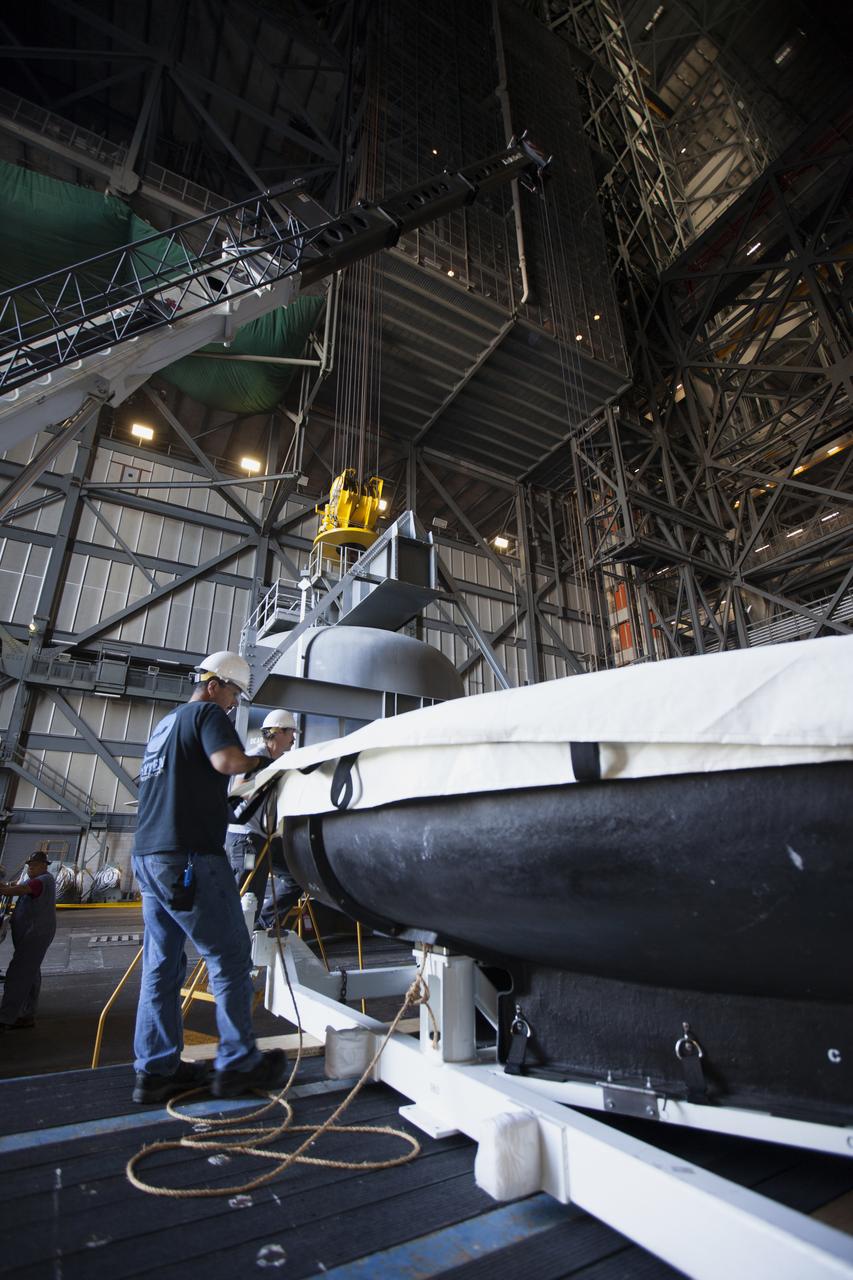 Inside High Bay 2 in the Vehicle Assembly Building (VAB) at NASA's Kennedy Space Center in Florida, workers help prepare the Orion heat shield from Exploration Flight Test-1 for unloading off its transporter. The heat shield is being transferred from the Orion Program to the Ground Systems Development and Operations Program, Landing and Recovery Operations. In the VAB, the heat shield will be integrated with the Orion ground test article and used for future underway recovery testing.