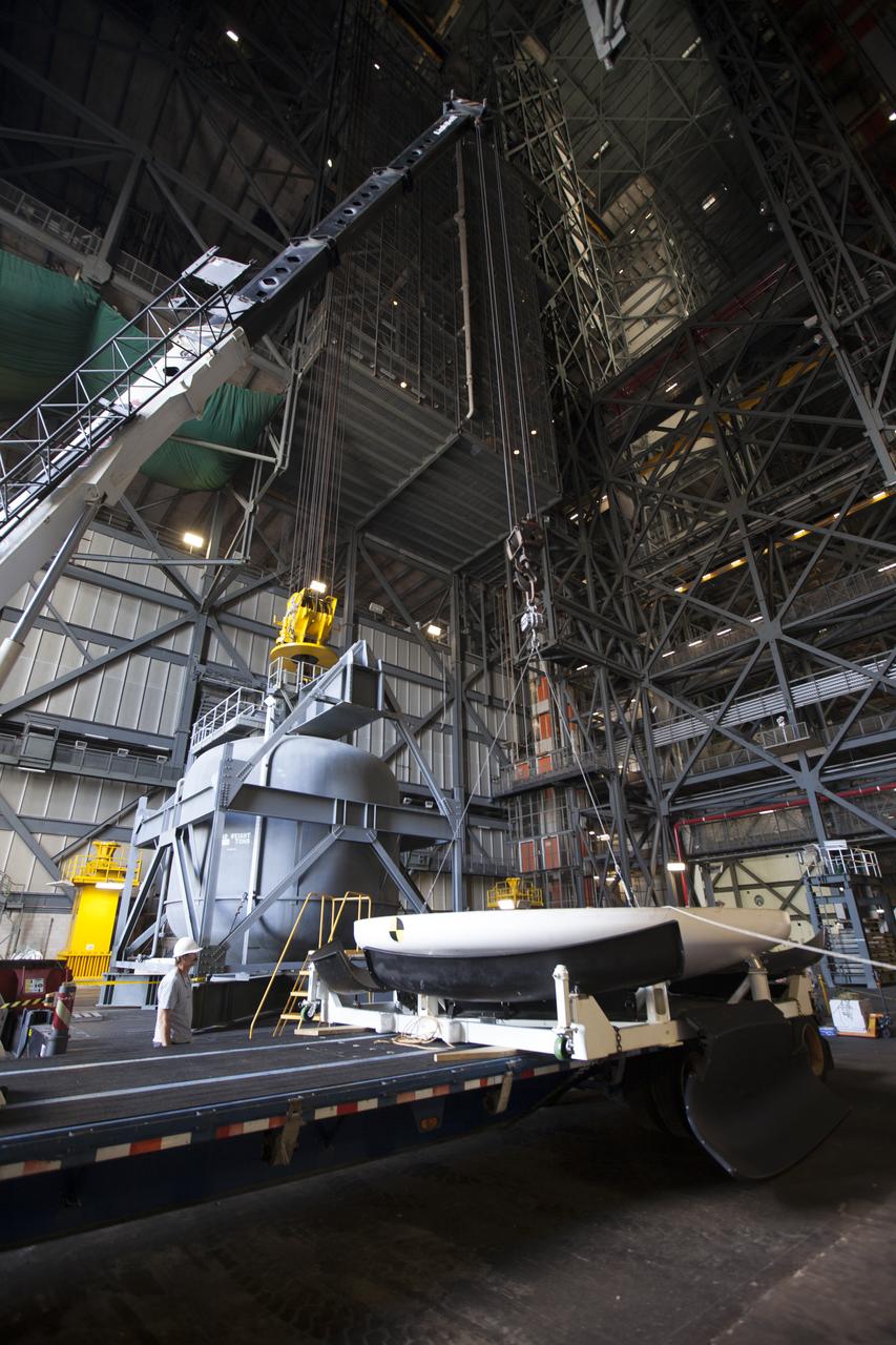Inside High Bay 2 in the Vehicle Assembly Building (VAB) at NASA's Kennedy Space Center in Florida, a crane is attached to the Orion heat shield from Exploration Flight Test-1 for unloading off its transporter. The heat shield is being transferred from the Orion Program to the Ground Systems Development and Operations Program, Landing and Recovery Operations. In the VAB, the heat shield will be integrated with the Orion ground test article and used for future underway recovery testing.