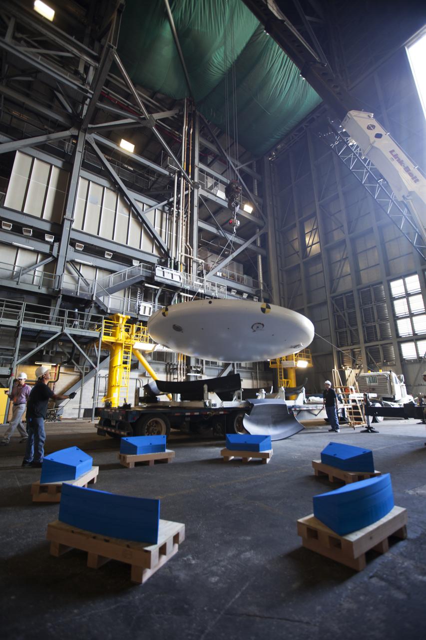 Inside High Bay 2 in the Vehicle Assembly Building (VAB) at NASA's Kennedy Space Center in Florida, a crane lifts the Orion heat shield from Exploration Flight Test-1 up off its transporter. It will be lowered onto foam blocks. The heat shield is being transferred from the Orion Program to the Ground Systems Development and Operations Program, Landing and Recovery Operations. In the VAB, the heat shield will be integrated with the Orion ground test article and used for future underway recovery testing.