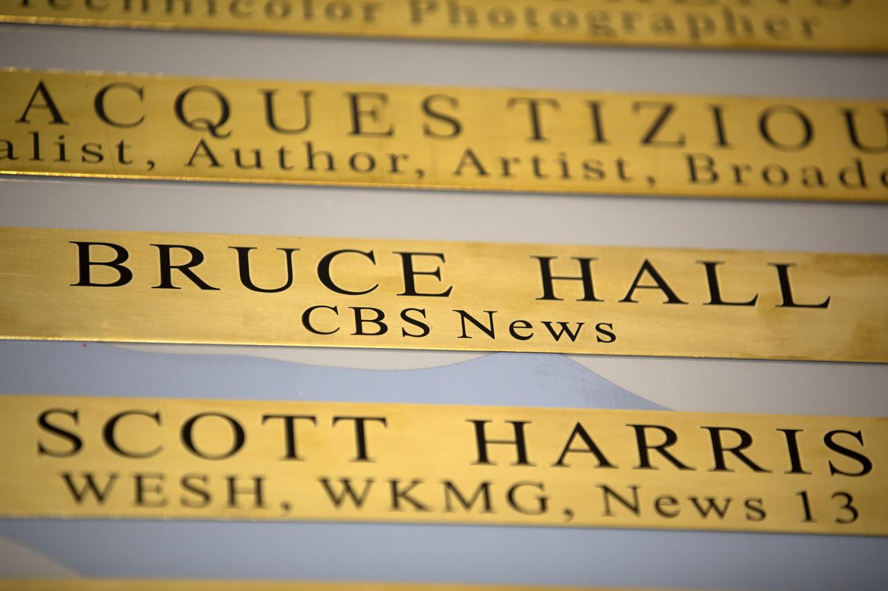 A brass plaque engraved with the name of Bruce Hall of CBS News is among the list of "The Chroniclers," a roll of honor on the wall at the NASA News Center at Kennedy Space Center in Florida. Hall, one of six new inductees in 2017, died after a lengthy illness on May 2, 2017. In this facility reporters from television, radio, print and online media outlets have monitored countless launches, landings and other space events in order to deliver the news to the world. The Chroniclers program recognizes retirees of the news and communications business who helped spread news of American space exploration from Kennedy Space Center for ten years or more. 