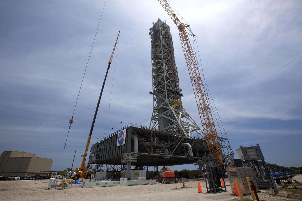 Several heavy lift cranes surround the mobile launcher at NASA's Kennedy Space Center in Florida. Preparations are underway to lift a vehicle support post up and onto the mobile launcher for installation on the deck. A total of eight support posts will be installed to support the load of the Space Launch System's (SLS) solid rocket boosters, with four posts for each of the boosters. The support posts are about five feet tall and each weigh about 10,000 pounds. The posts will structurally support the SLS rocket through T-0 and liftoff, and will drop down before vehicle liftoff to avoid contact with the flight hardware. The Ground Systems Development and Operations Program is overseeing installation of the support posts to prepare for the launch of the Orion spacecraft atop the SLS rocket. 