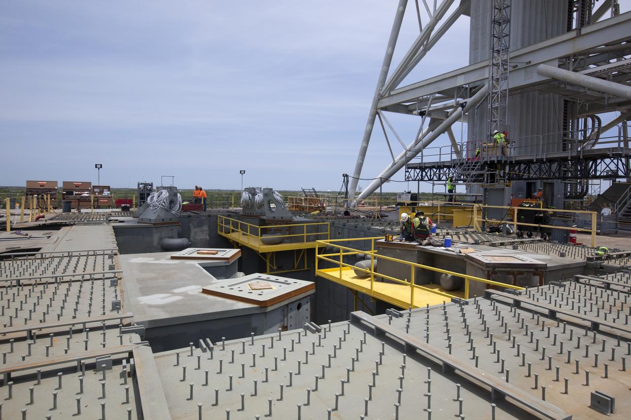 Construction workers on the deck of the mobile launcher prepare the platforms for installation of vehicle support posts at NASA's Kennedy Space Center in Florida. At left, four of the support posts are installed. A total of eight support posts will be installed to support the load of the Space Launch System's (SLS) solid rocket boosters, with four posts for each of the boosters. The support posts are about five feet tall and each weigh about 10,000 pounds. The posts will structurally support the SLS rocket through T-0 and liftoff, and will drop down before vehicle liftoff to avoid contact with the flight hardware. The Ground Systems Development and Operations Program is overseeing installation of the support posts to prepare for the launch of the Orion spacecraft atop the SLS rocket.