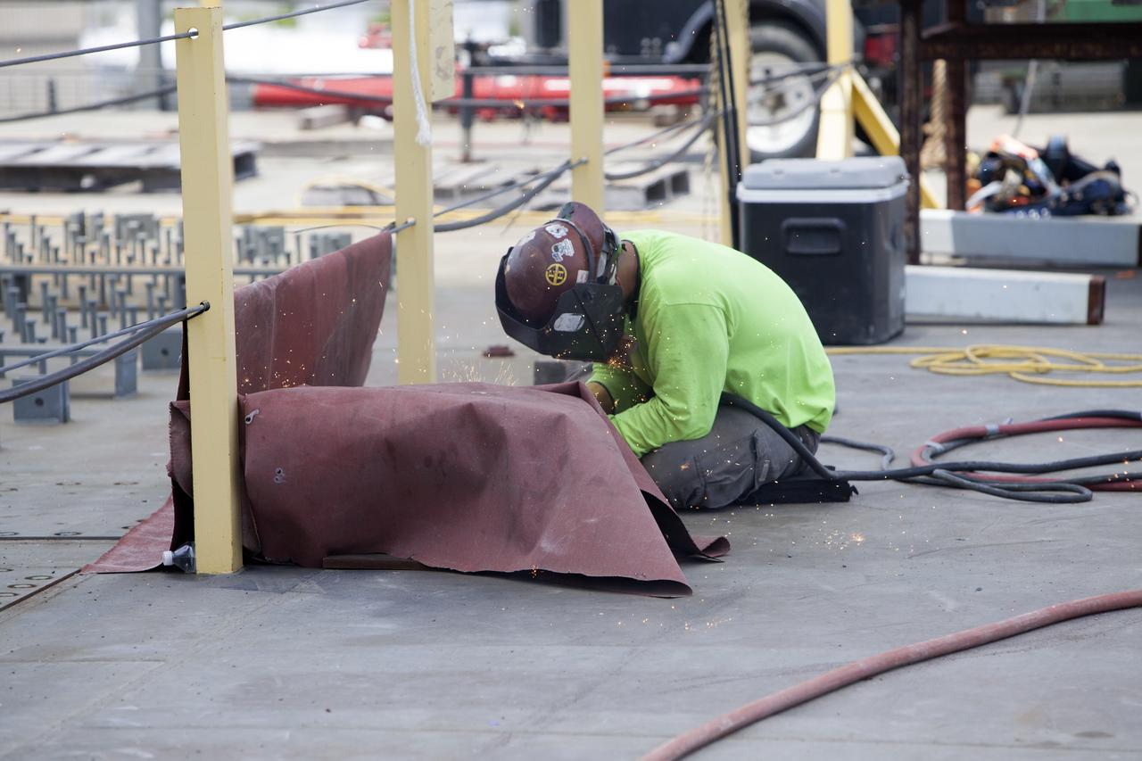 A construction worker on the deck of the mobile launcher welds a portion of a platform for installation of a vehicle support post at NASA's Kennedy Space Center in Florida. A total of eight support posts will be installed to support the load of the Space Launch System's (SLS) solid rocket boosters, with four posts for each of the boosters. The support posts are about five feet tall and each weigh about 10,000 pounds. The posts will structurally support the SLS rocket through T-0 and liftoff, and will drop down before vehicle liftoff to avoid contact with the flight hardware. The Ground Systems Development and Operations Program is overseeing installation of the support posts to prepare for the launch of the Orion spacecraft atop the SLS rocket. 