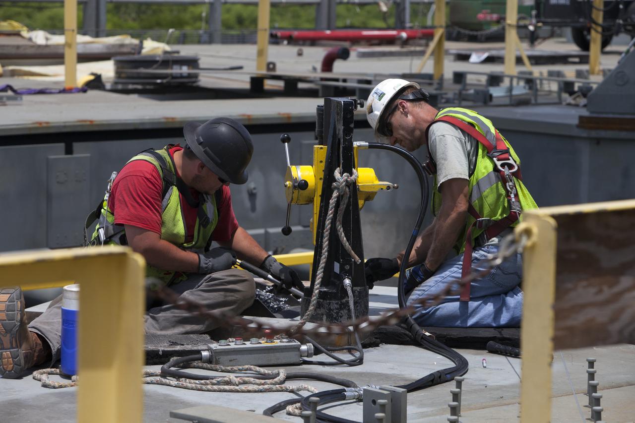 Construction workers on the deck of the mobile launcher at NASA's Kennedy Space Center in Florida, prepare a platform for installation of a vehicle support post. A total of eight support posts will be installed to support the load of the Space Launch System's (SLS) solid rocket boosters, with four posts for each of the boosters. The support posts are about five feet tall and each weigh about 10,000 pounds. The posts will structurally support the SLS rocket through T-0 and liftoff, and will drop down before vehicle liftoff to avoid contact with the flight hardware. The Ground Systems Development and Operations Program is overseeing installation of the support posts to prepare for the launch of the Orion spacecraft atop the SLS rocket.