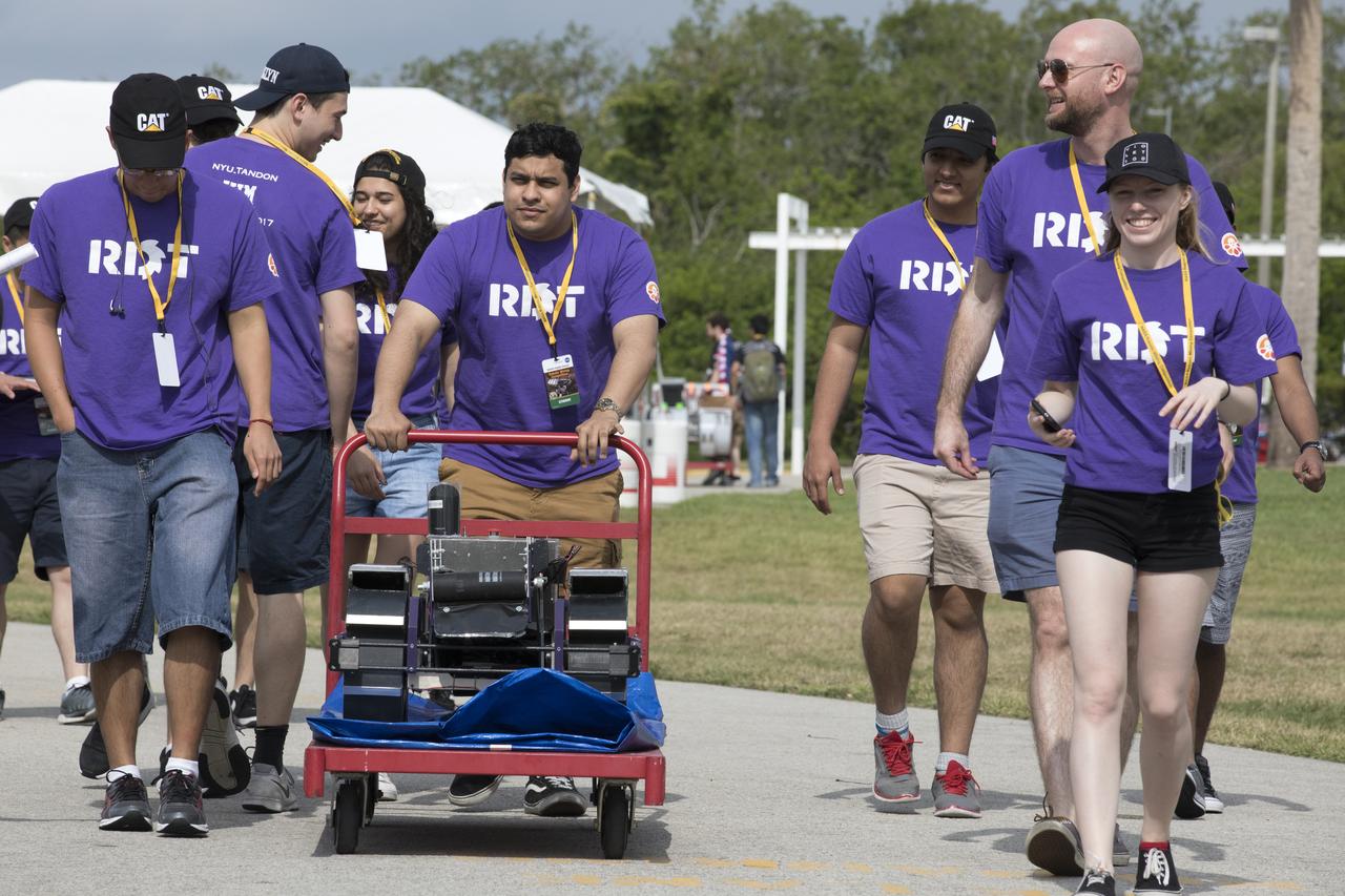 Team members from the New York University Tandon School of Engineering transport their robot to the mining arena during NASA's 8th Annual Robotic Mining Competition at the Kennedy Space Center Visitor Complex in Florida. More than 40 student teams from colleges and universities around the U.S. are using their uniquely-designed mining robots to dig in a supersized sandbox filled with BP-1, or simulated Martian soil, and participate in other competition requirements. The Robotic Mining Competition is a NASA Human Exploration and Operations Mission Directorate project designed to encourage students in science, technology, engineering and math, or STEM fields. The project provides a competitive environment to foster innovative ideas and solutions that could be used on NASA's Journey to Mars. 