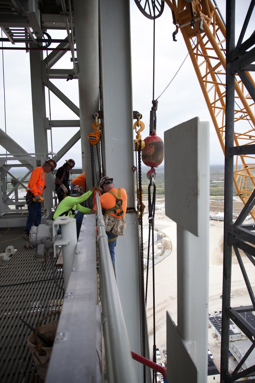 Construction workers assist as a crane lifts the Core Stage Forward Skirt Umbilical into position for installation on the mobile launcher tower at NASA's Kennedy Space Center in Florida. The mobile launcher tower will be equipped with a number of lines, called umbilicals that will connect to the Space Launch System (SLS) rocket and Orion spacecraft for Exploration Mission-1 (EM-1). The CSFSU will be located at about the 180-foot level on the tower, above the liquid oxygen tank. The CSFSU is an umbilical that will swing into position to provide connections to the core stage forward skirt of the SLS rocket, and then swing away before launch. Its main purpose is to provide conditioned air/GN2 to the SLS core stage forward skirt cavity. The Ground Systems Development and Operations Program is overseeing installation of the umbilicals. 