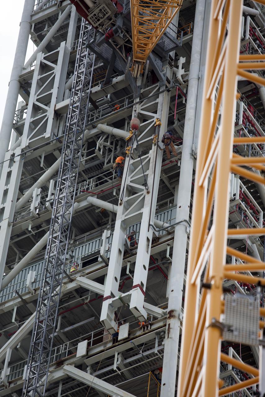 Construction workers assist as a crane lifts the Core Stage Forward Skirt Umbilical into position for installation on the mobile launcher tower at NASA's Kennedy Space Center in Florida. The mobile launcher tower will be equipped with a number of lines, called umbilicals that will connect to the Space Launch System (SLS) rocket and Orion spacecraft for Exploration Mission-1 (EM-1). The CSFSU will be located at about the 180-foot level on the tower, above the liquid oxygen tank. The CSFSU is an umbilical that will swing into position to provide connections to the core stage forward skirt of the SLS rocket, and then swing away before launch. Its main purpose is to provide conditioned air/GN2 to the SLS core stage forward skirt cavity. The Ground Systems Development and Operations Program is overseeing installation of the umbilicals. 