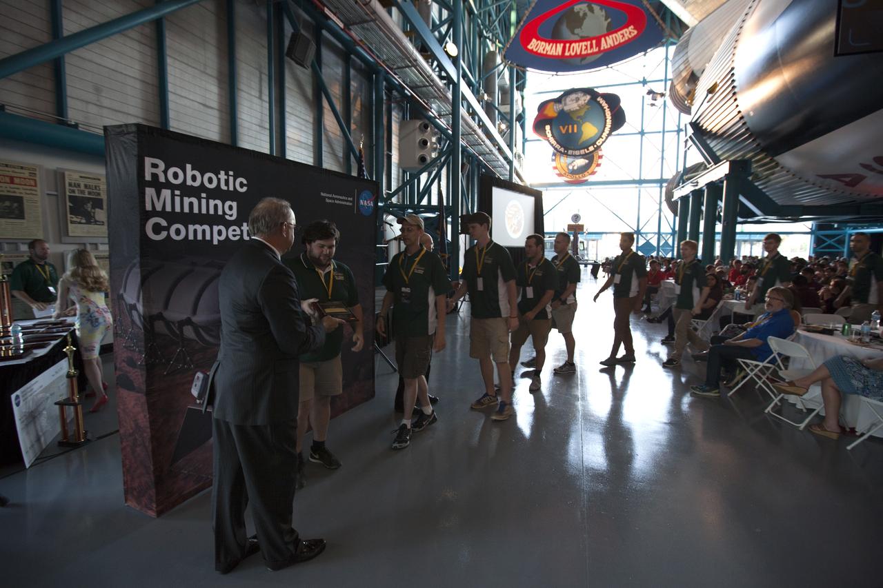 Inside the Apollo-Saturn V Center at the Kennedy Space Center Visitor Complex in Florida, team members from the University of North Carolina at Charlotte receive third-place in the Caterpillar Autonomy Award during the award ceremony for NASA's 8th Annual Robotic Mining Competition. More than 40 student teams from colleges and universities around the U.S. used their uniquely-designed mining robots to dig in a supersized sandbox filled with BP-1, or simulated Martian soil, and participated in other competition requirements, May 22-26, at the visitor complex. The Robotic Mining Competition is a NASA Human Exploration and Operations Mission Directorate project designed to encourage students in science, technology, engineering and math, or STEM fields. The project provides a competitive environment to foster innovative ideas and solutions that could be used on NASA's Journey to Mars.
