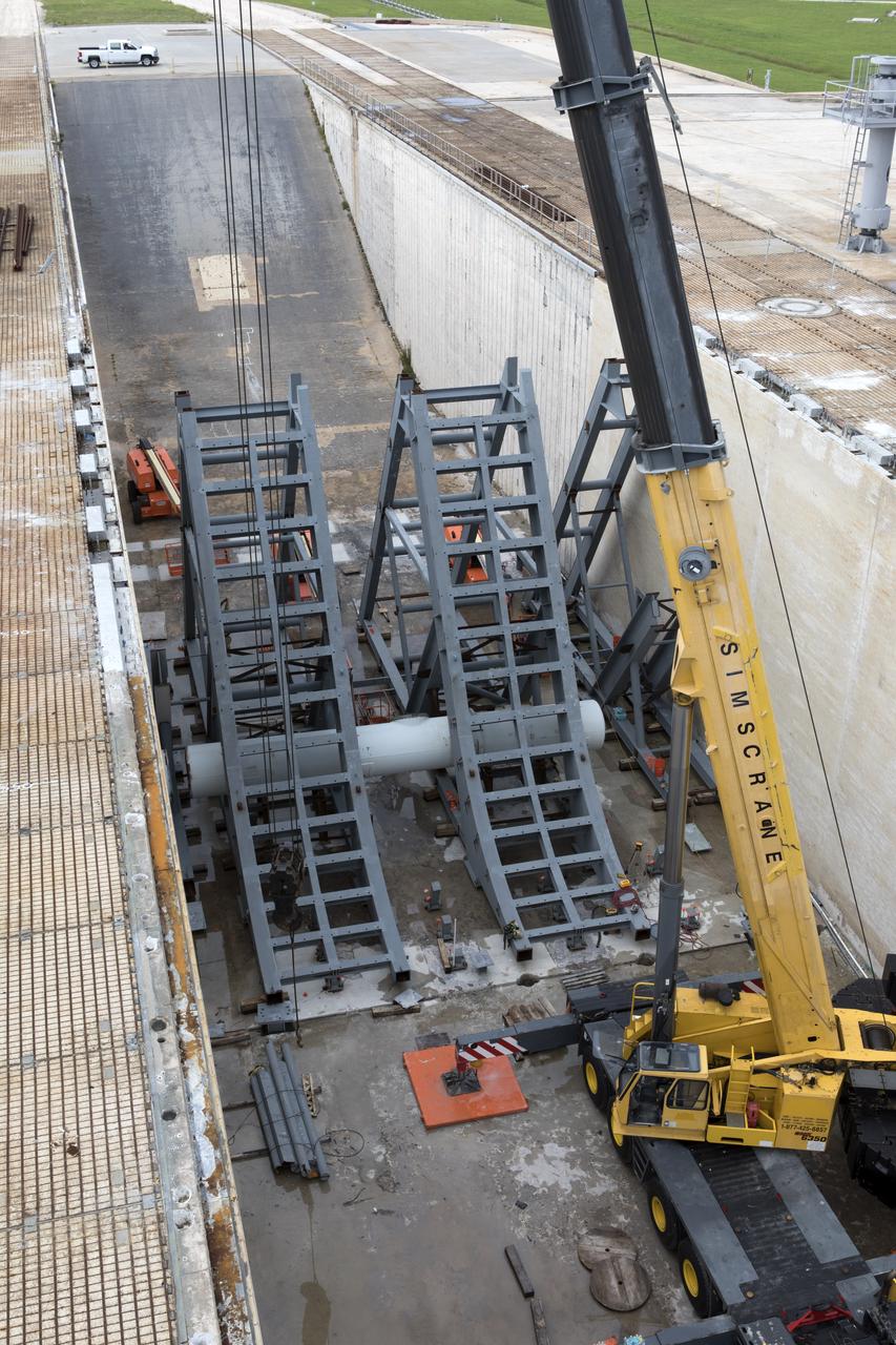 In a view from above at Launch Pad 39B at NASA's Kennedy Space Center in Florida, construction workers position large segments of the support hardware for a new flame deflector in the flame trench. The new flame deflector will be positioned about six feet south of the shuttle-era flame deflector’s position. During liftoff of NASA’s Space Launch System, the rocket’s flame and energy will be diverted to the north side of the flame trench. The north side of the deflector will be protected by a NASA standard coating. The south side of the deflector will not be slanted and will have no lining. The new design will provide easier access for inspection, maintenance and repair. The Ground Systems Development and Operations (GSDO) Program at Kennedy is managing the installation of the flame deflector for Exploration Mission 1, deep space missions, and NASA's Journey to Mars. 
