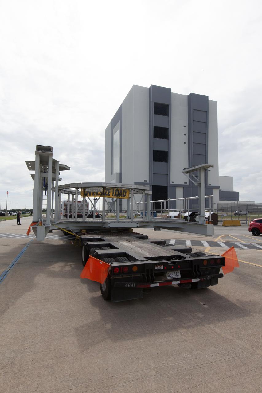 A flatbed truck carrying one of two new service platforms for NASA's Space Launch System booster engines arrives at the Vehicle Assembly Building (VAB) at the agency's Kennedy Space Center in Florida. The platforms were transported from fabricator Met-Con Inc. in Cocoa, Florida. They will be stored in the VAB, where they will be used for processing and checkout of the engines for the rocket's twin five-segment solid rocket boosters for Exploration Mission-1. EM-1 will launch an uncrewed Orion spacecraft to a stable orbit beyond the Moon and bring it back to Earth for a splashdown in the Pacific Ocean.