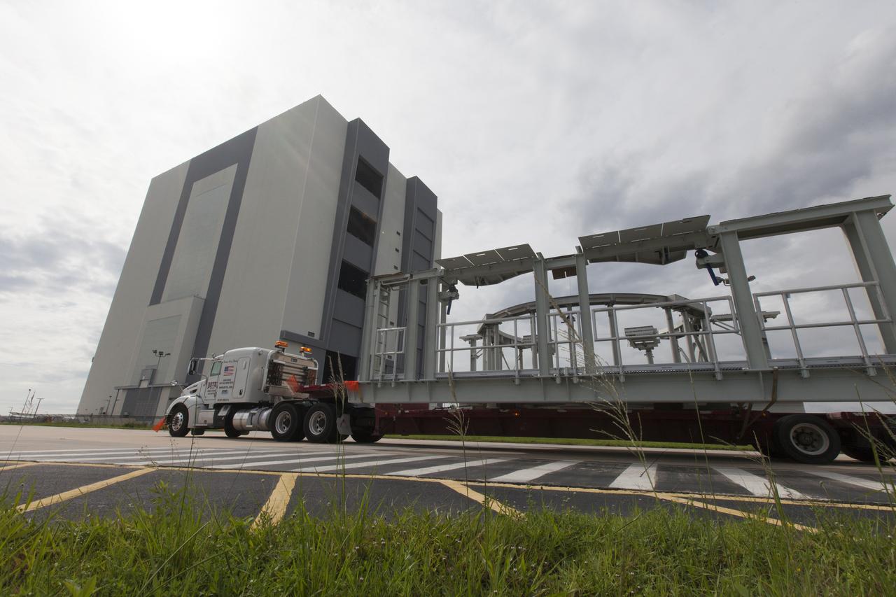 A flatbed truck carrying one of two new service platforms for NASA's Space Launch System booster engines arrives at the Vehicle Assembly Building (VAB) at the agency's Kennedy Space Center in Florida. The platforms were transported from fabricator Met-Con Inc. in Cocoa, Florida. They will be stored in the VAB, where they will be used for processing and checkout of the engines for the rocket's twin five-segment solid rocket boosters for Exploration Mission-1. EM-1 will launch an uncrewed Orion spacecraft to a stable orbit beyond the Moon and bring it back to Earth for a splashdown in the Pacific Ocean.