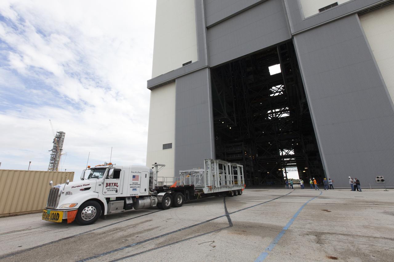 A flatbed truck carrying one of two new service platforms for NASA's Space Launch System booster engines backs in to the Vehicle Assembly Building (VAB) at the agency's Kennedy Space Center in Florida. The platforms were transported from fabricator Met-Con Inc. in Cocoa, Florida. They will be stored in the VAB, where they will be used for processing and checkout of the engines for the rocket's twin five-segment solid rocket boosters for Exploration Mission-1. EM-1 will launch an uncrewed Orion spacecraft to a stable orbit beyond the Moon and bring it back to Earth for a splashdown in the Pacific Ocean.