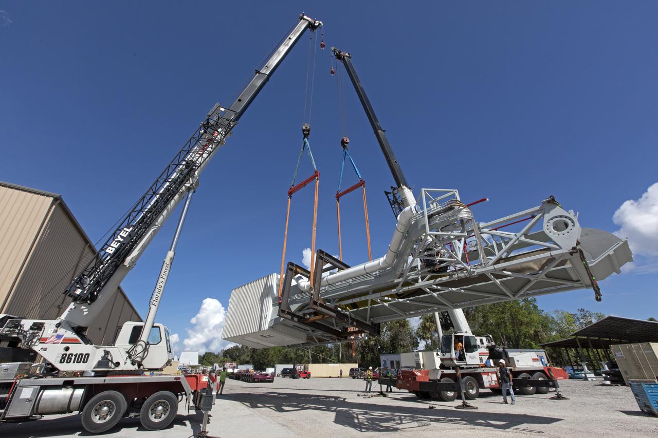 Two heavy-lift cranes are being used to move the Orion crew access arm and lower it onto a flatbed truck at Precision Fabricating and Cleaning in Cocoa, Florida. The crew access arm will be transported to a storage location near NASA's Kennedy Space Center in Florida. Later this month, the arm will be transported to the mobile launcher (ML) tower at the center. The crew access arm will be located at about the 274-foot level on the tower. It will rotate from its retracted position and interface with the Orion crew hatch location to provide entry to the Orion crew module. The Ground Systems Development and Operations Program is overseeing installation of umbilicals and launch accessories on the ML tower.