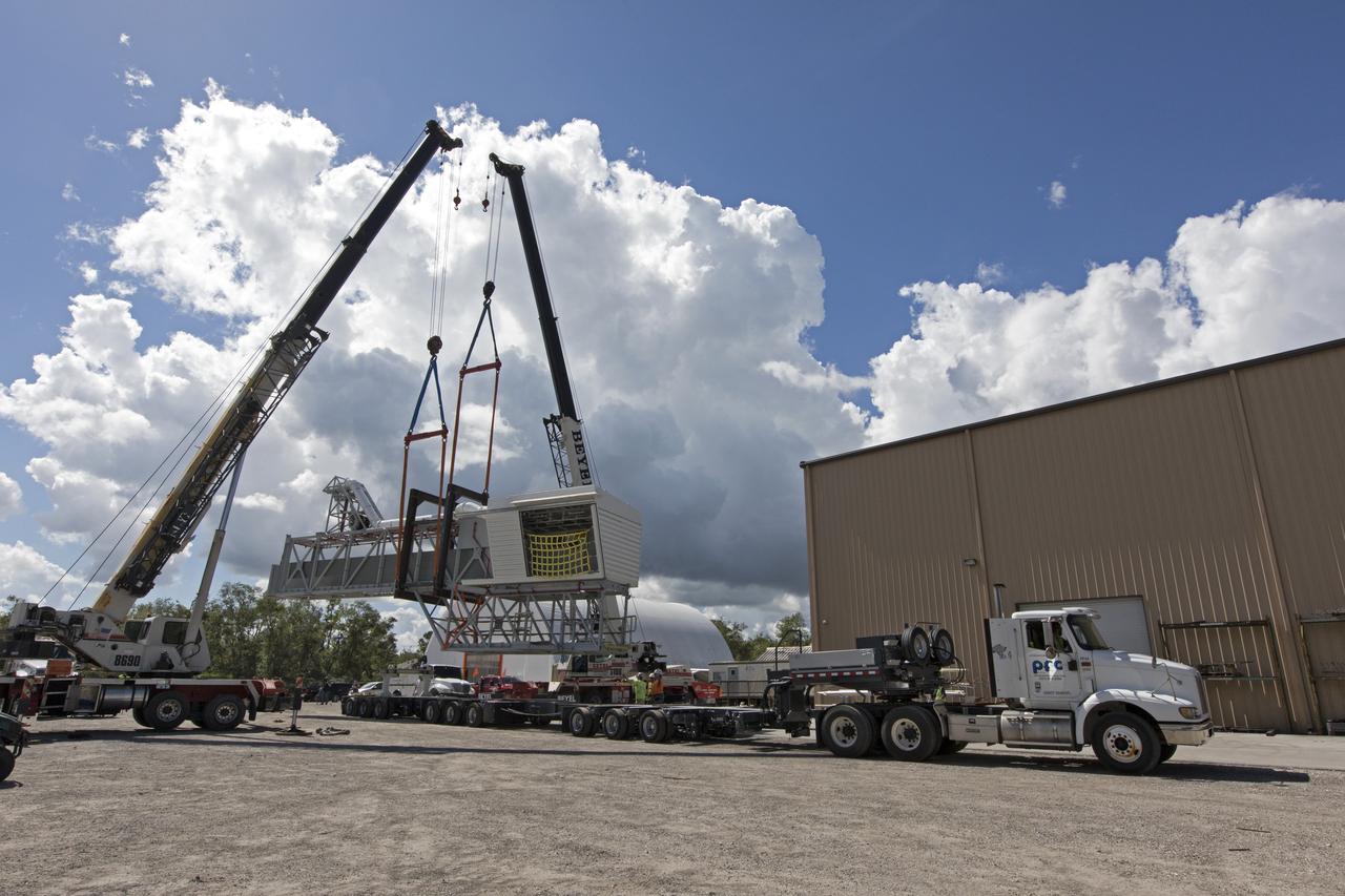 Two heavy-lift cranes are being used to lower the Orion crew access arm onto a flatbed truck at Precision Fabricating and Cleaning in Cocoa, Florida. The crew access arm will be transported to a storage location near NASA's Kennedy Space Center in Florida. Later this month, the arm will be transported to the mobile launcher (ML) tower at the center. The crew access arm will be located at about the 274-foot level on the tower. It will rotate from its retracted position and interface with the Orion crew hatch location to provide entry to the Orion crew module. The Ground Systems Development and Operations Program is overseeing installation of umbilicals and launch accessories on the ML tower.