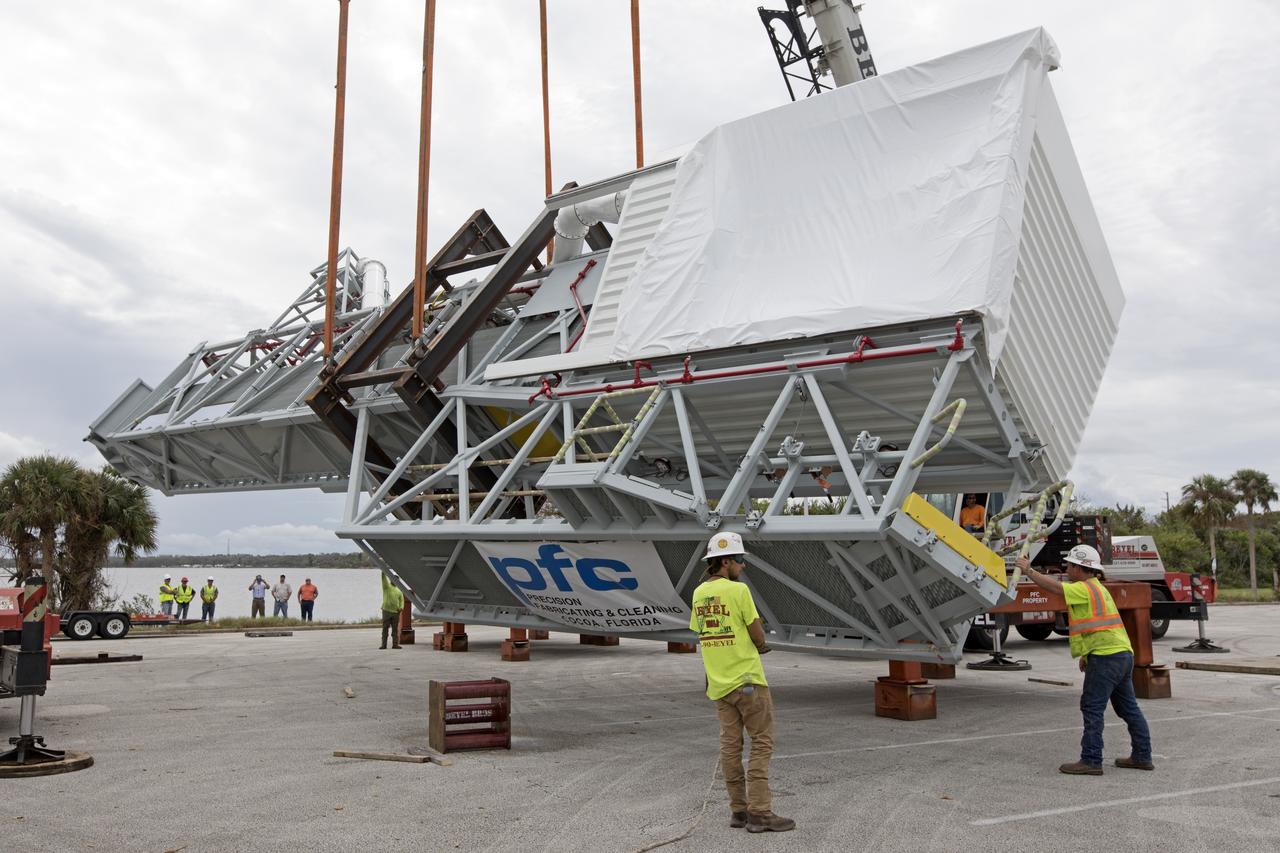 Two heavy-lift cranes are used to tilt and lower the Orion crew access arm onto a work stand in a storage location at NASA's Kennedy Space Center in Florida. The access arm was transported from Precision Fabricating and Cleaning in Cocoa, Florida. Later this month, the arm will be transported to the mobile launcher (ML) tower at the center. The crew access arm will be located at about the 274-foot level on the tower. It will rotate from its retracted position and interface with the Orion crew hatch location to provide entry to the Orion crew module. The Ground Systems Development and Operations Program is overseeing installation of umbilicals and launch accessories on the ML tower. 