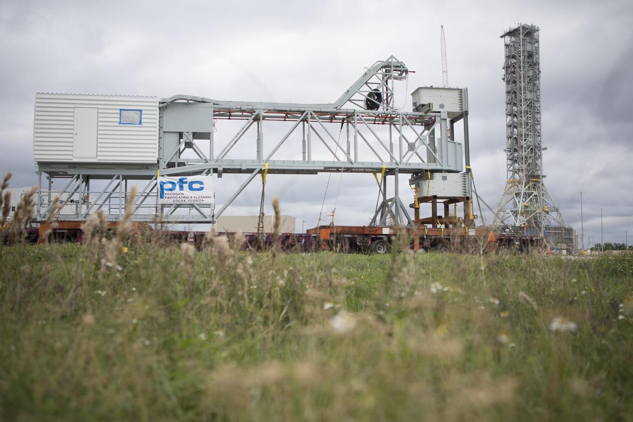 A heavy-load transport truck carrying the Orion crew access arm nears the mobile launcher (ML) at NASA's Kennedy Space Center in Florida. The crew access arm will be installed at about the 274-foot level on the mobile launcher tower. It will rotate from its retracted position and interface with the Orion crew hatch location to provide entry to the Orion crew module. The Ground Systems Development and Operations Program is overseeing installation of umbilicals and launch accessories on the ML tower to prepare for Exploration Mission-1. 